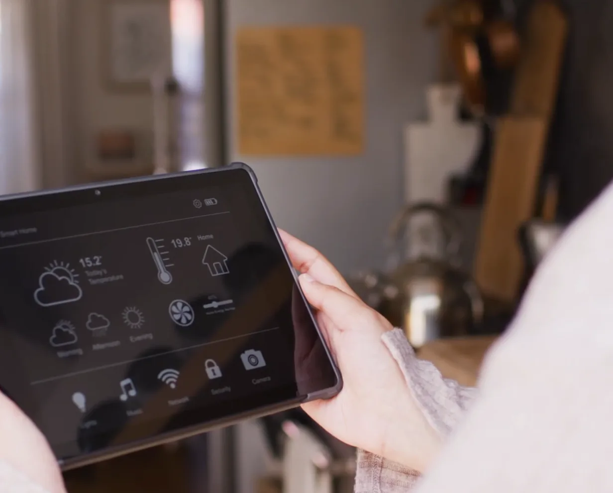 A hand holding a tablet that shows a home’s air, light and temperature controls.