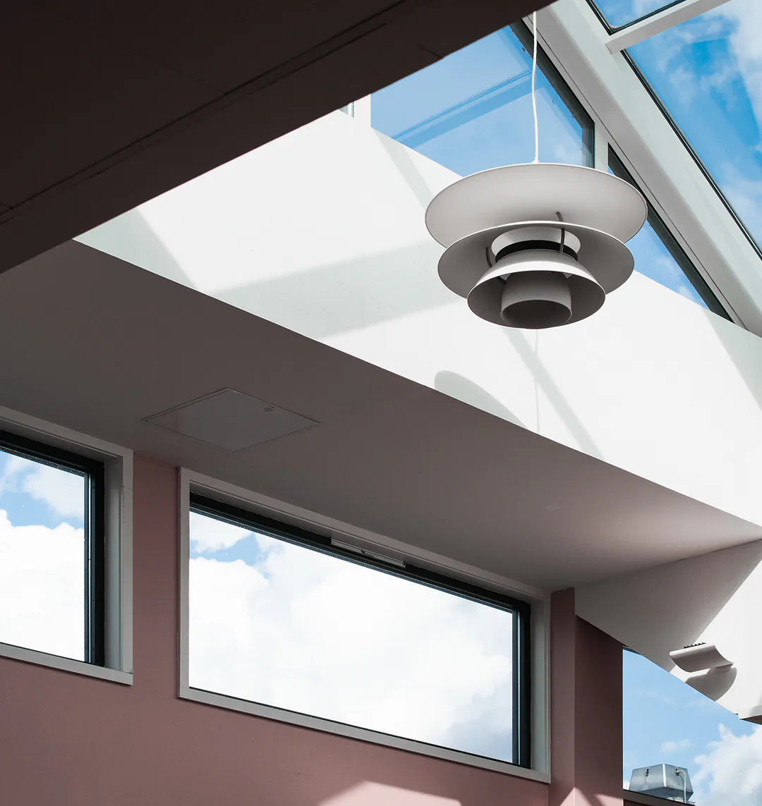 A pendant lamp under a skylight above a rose-coloured wall.