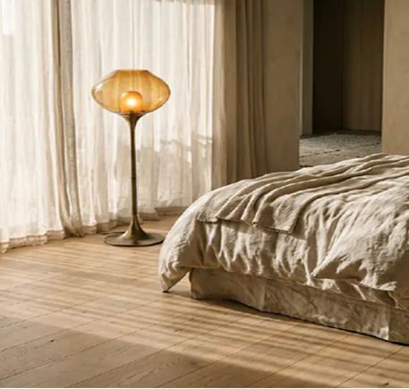 A warm amber lamp beside a linen-dressed bed.