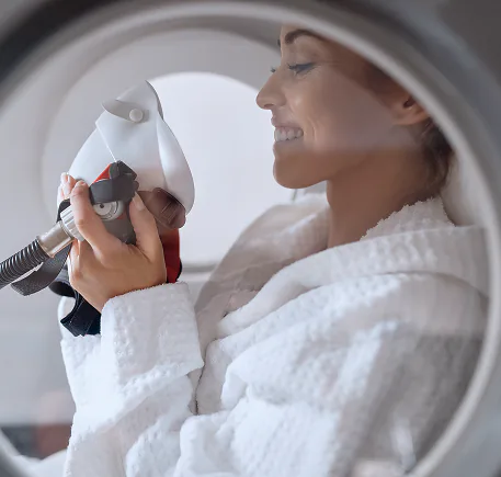 A guest in a white robe breathing through an oxygen mask inside a hyperbaric chamber.