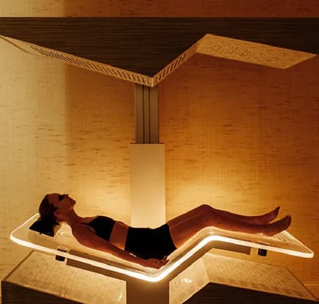 A guest reclining on a lit multi-therapy bed in a timber-lined cabin.