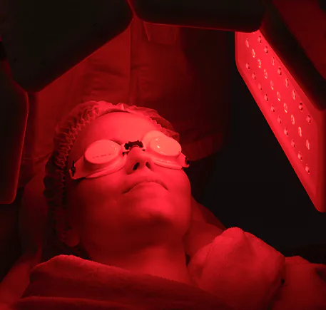 A guest in protective eyewear beneath a red light therapy panel.